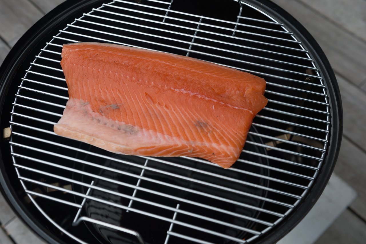 A large salmon fillet is placed on a round grill for smoking or grilling.