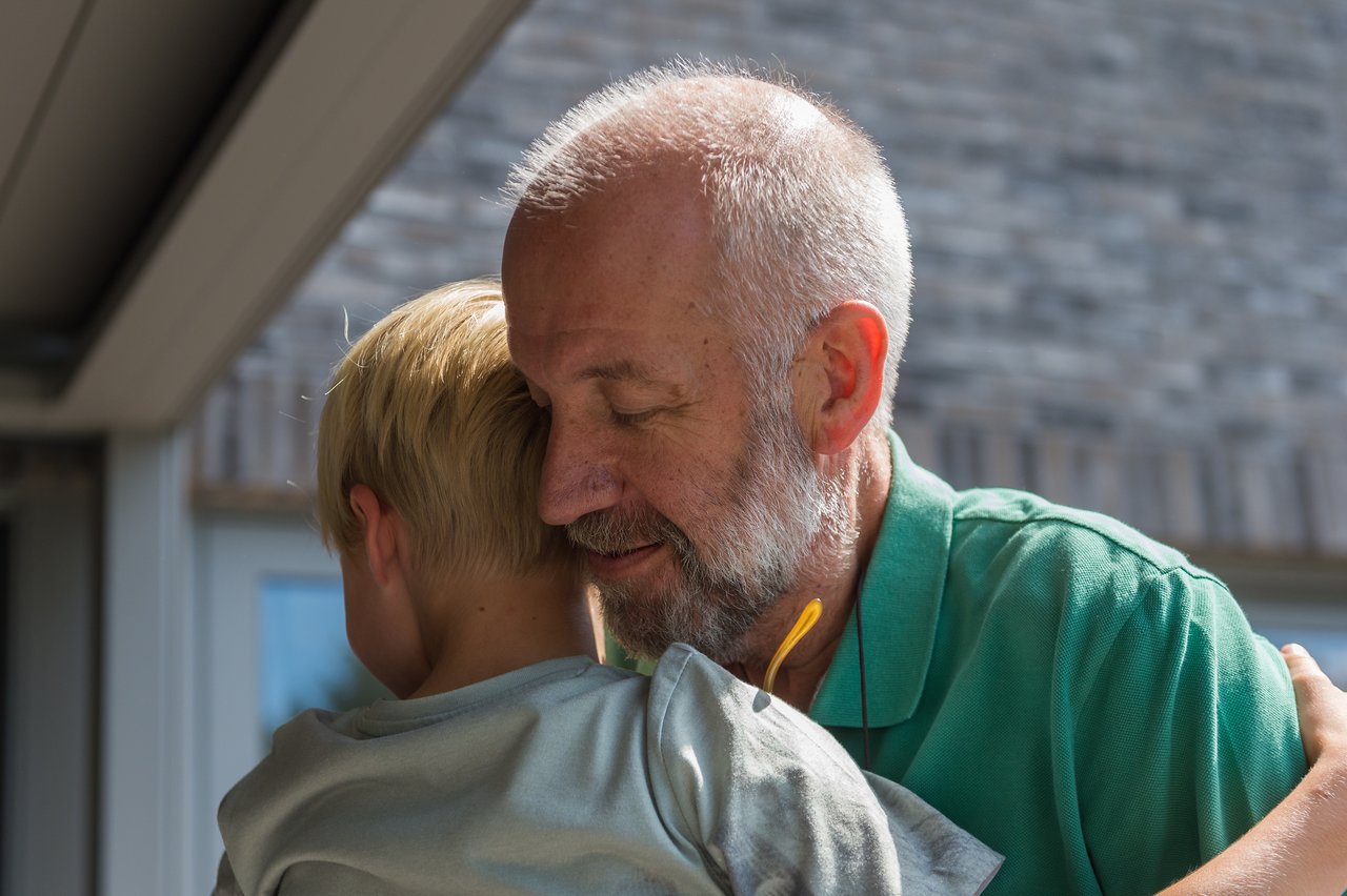 A child hugs their grandfather tightly while he smiles with his eyes closed.