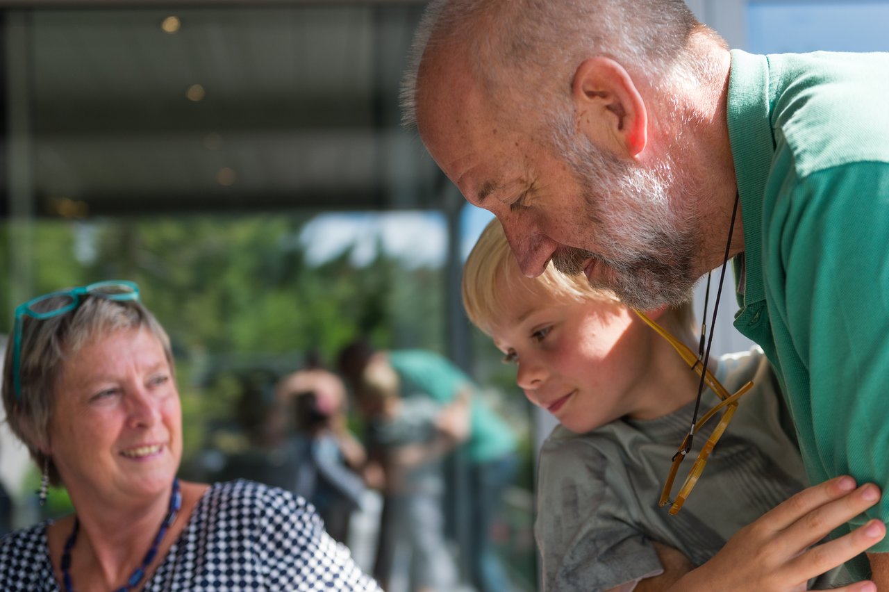 A young child hugs an older man while a woman nearby smiles and watches.