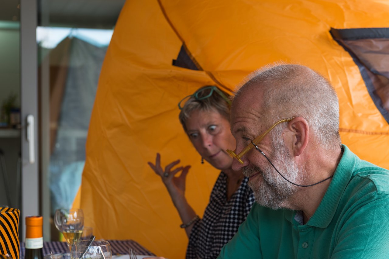 A man in a green shirt sits at a table, with part of a tent covering his head.
