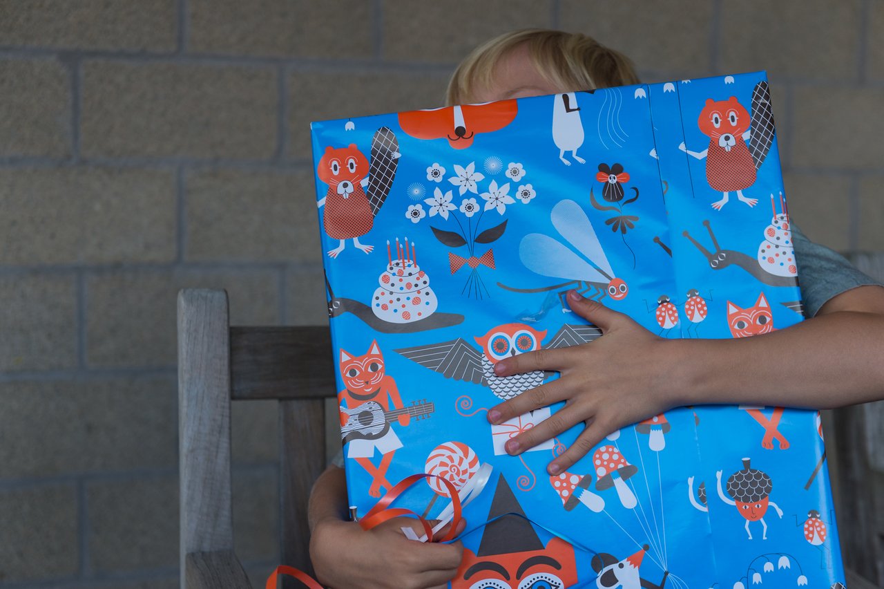 A child holds a large, brightly wrapped gift while starting to unwrap it.