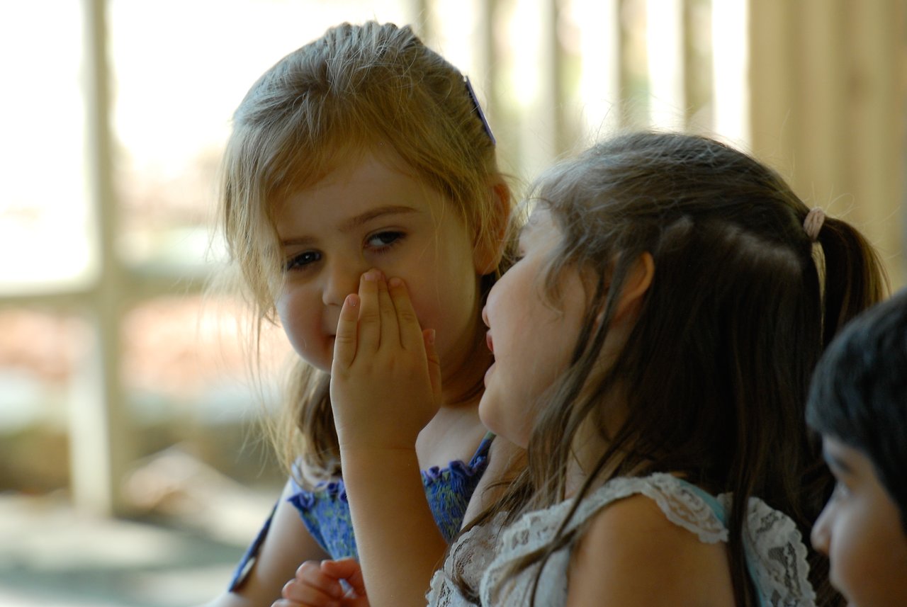 A young girl whispers into another girl's ear while they smile at a birthday party.