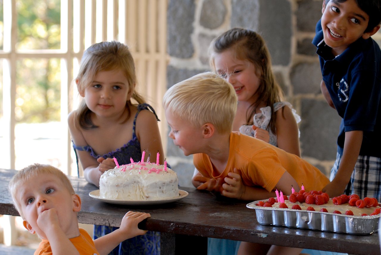 Children gather around a birthday cake with lit candles, laughing and excitedly preparing to celebrate.