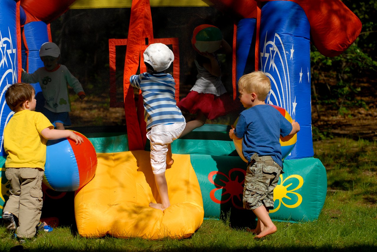 Children play with beach balls and climb into a colorful inflatable bounce house at an outdoor birthday party.