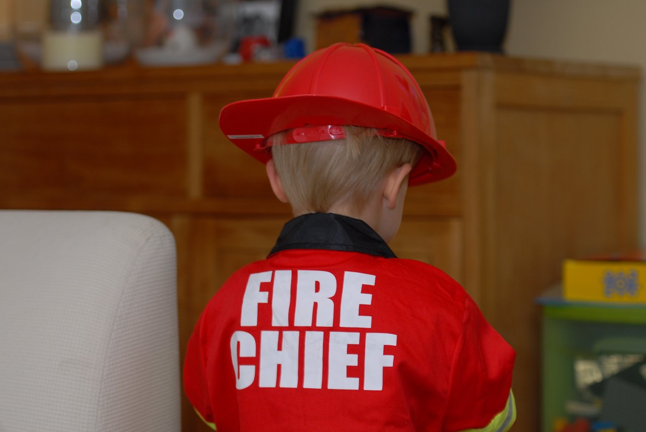 A child wearing a red firefighter costume and helmet stands with their back to the camera.