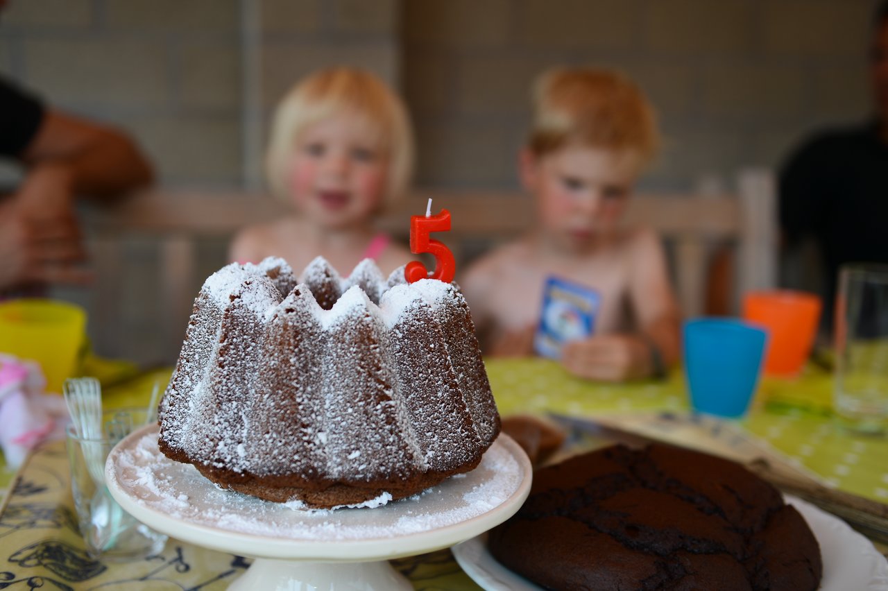 A chocolate cake with a red number 5 candle sits on a table at a birthday party.