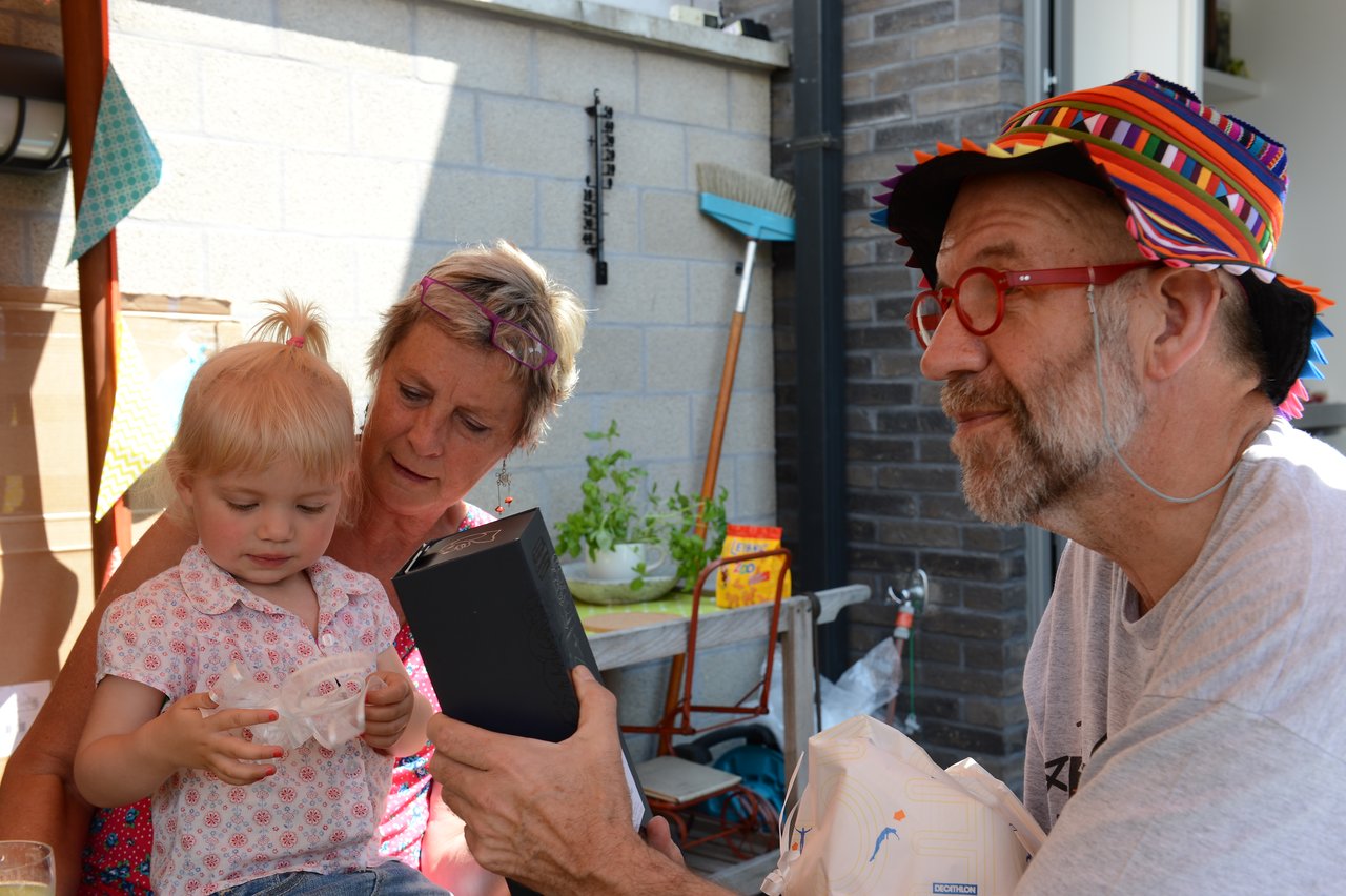 A man in a colorful hat shows a gift to a young child, while a woman watches closely.