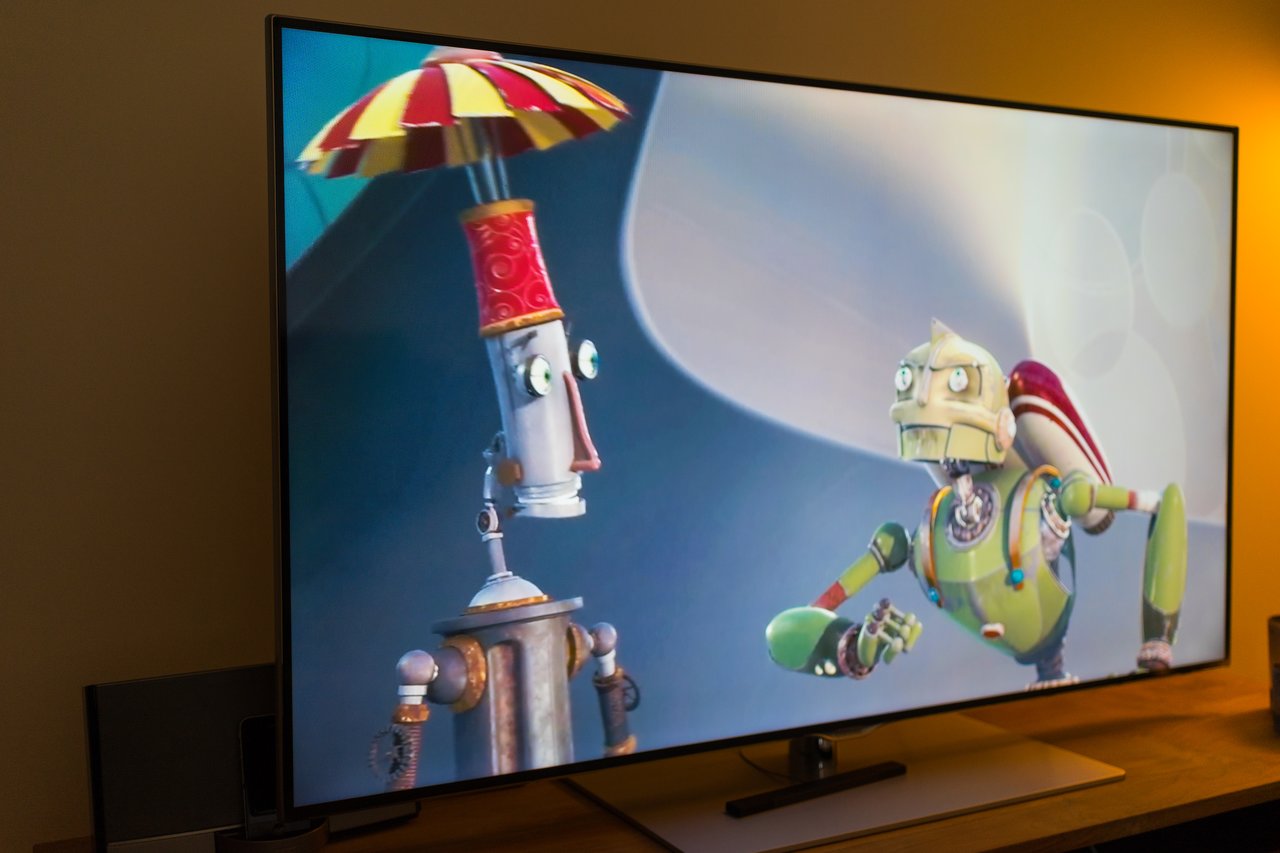 A television screen displays an animated movie scene featuring two colorful robot characters in conversation.