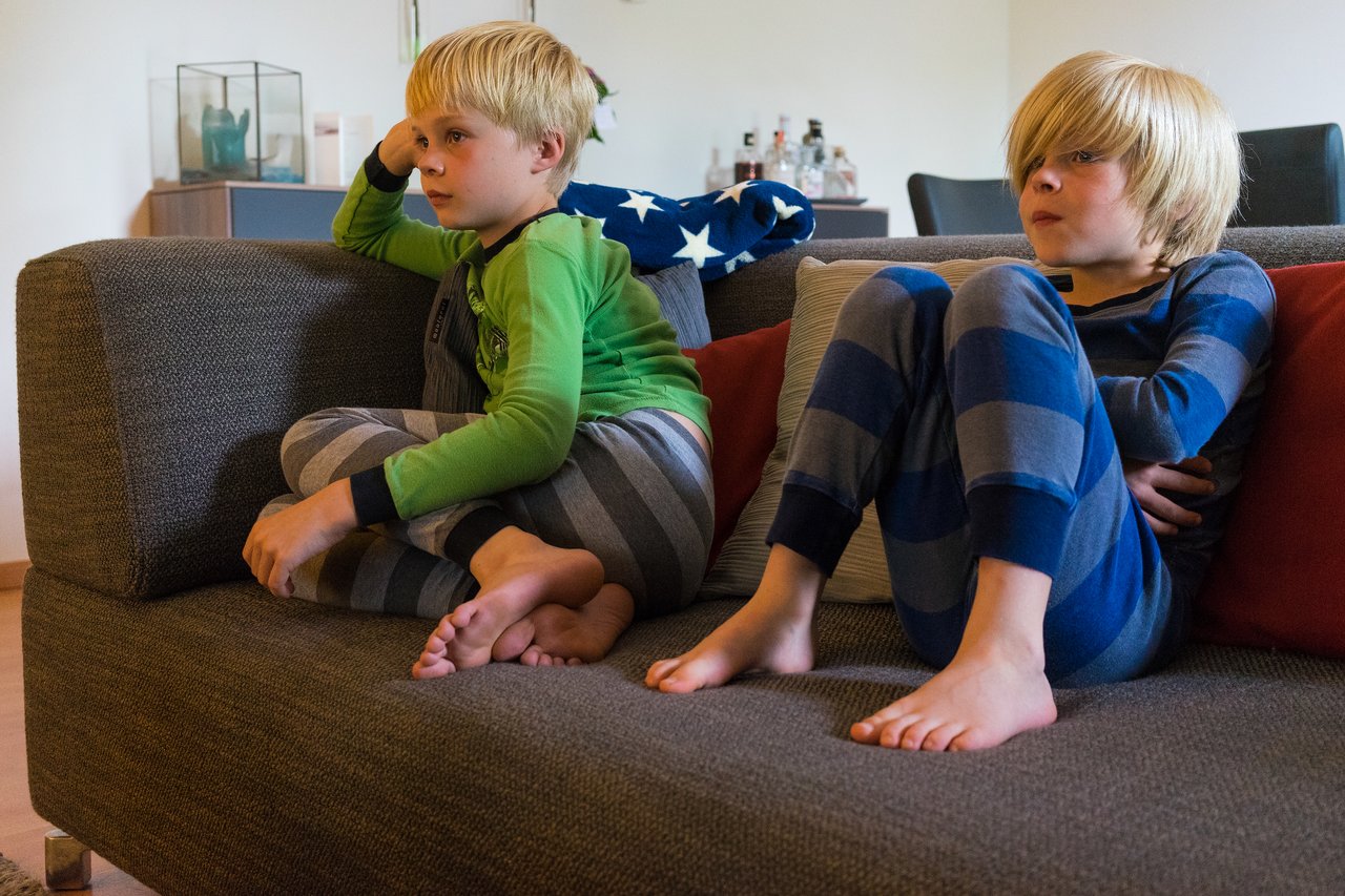 Two children in pajamas sit on a couch, watching something with focused expressions.