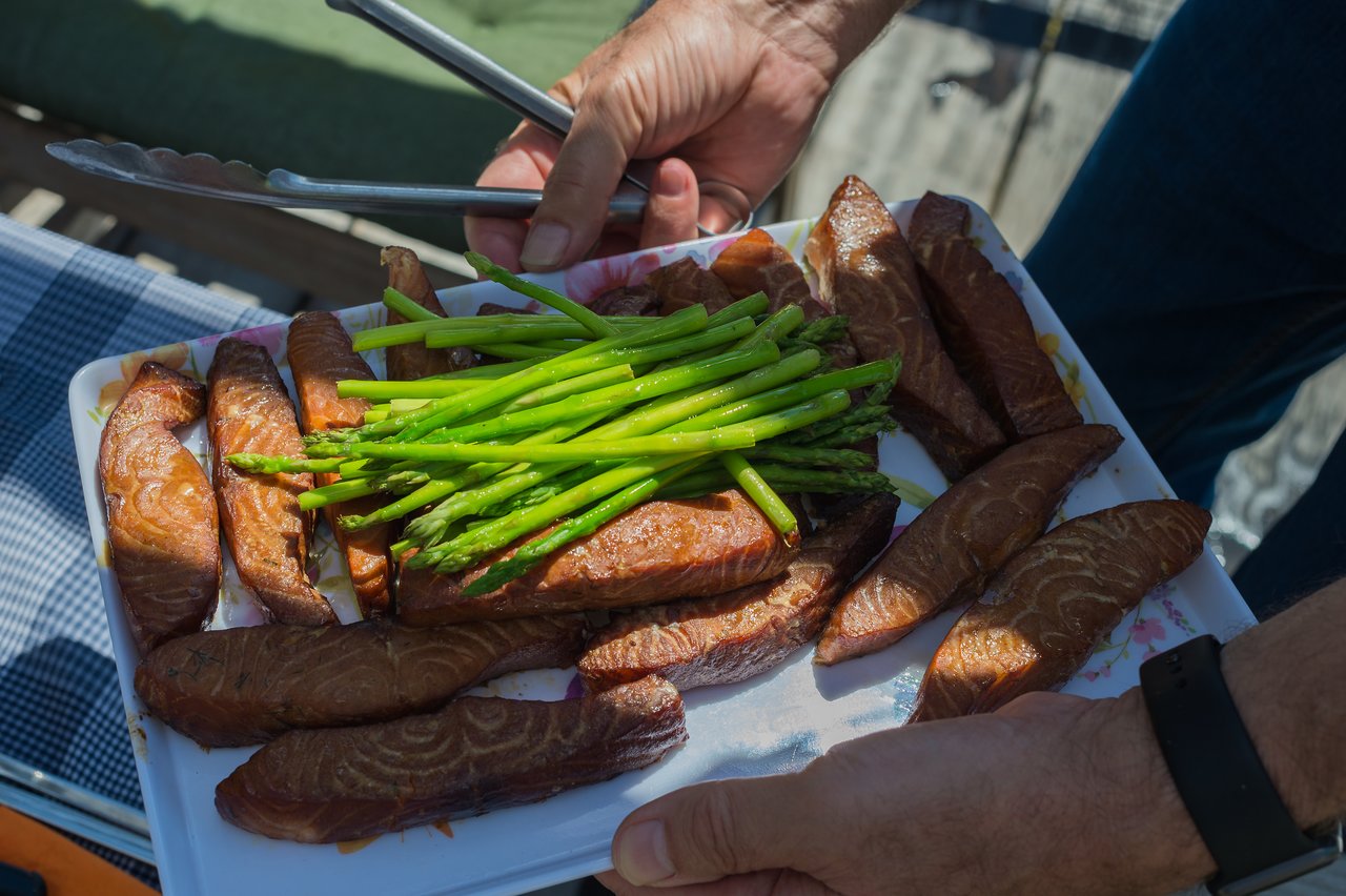 A person holds a plate of grilled salmon and asparagus, using tongs to serve the food.
