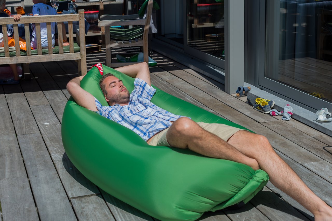 A man in a plaid shirt and shorts relaxes on a green inflatable lounger with his eyes closed.