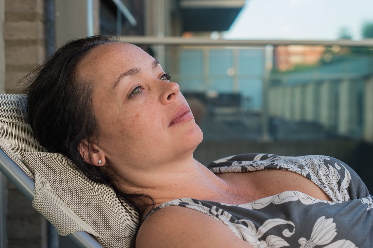 A woman reclines on a lounge chair on a deck, looking relaxed.