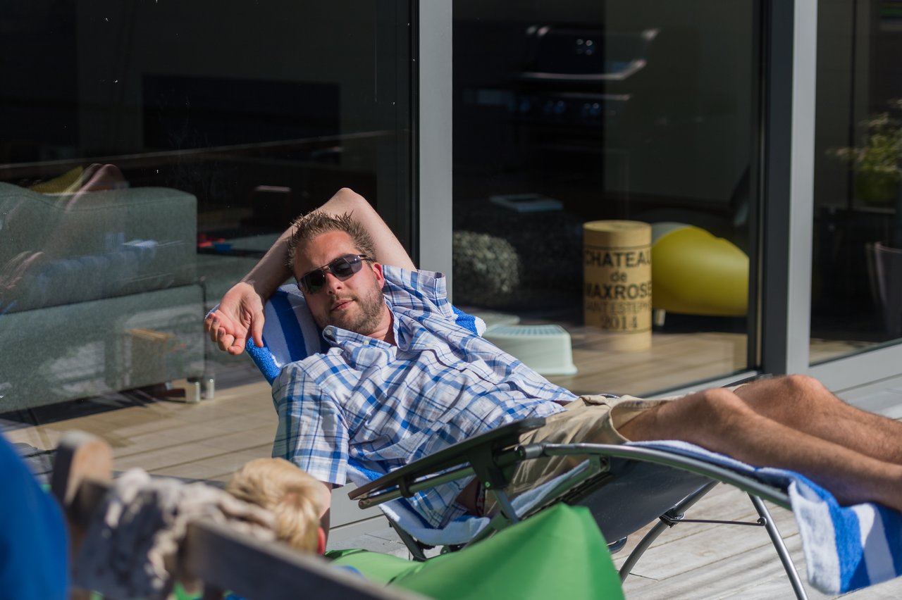 A man wearing sunglasses reclines on a lounge chair outdoors, resting with one arm behind his head.