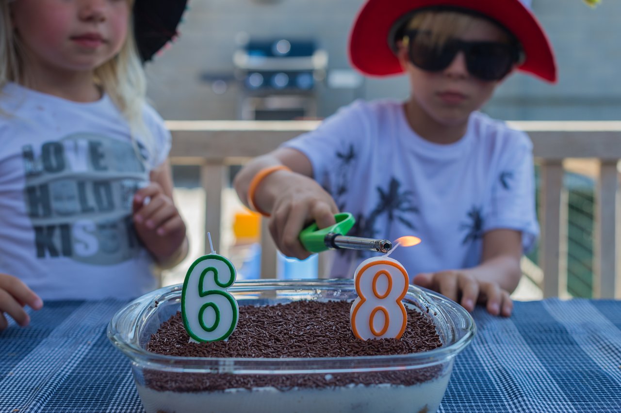 A child lights number candles on a birthday cake while another child watches nearby.
