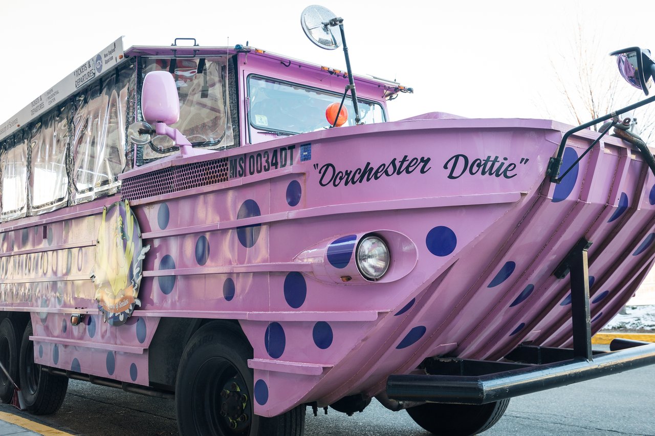 A pink and purple Boston Duck Tour vehicle named "Dorchester Dottie" is parked on the street.