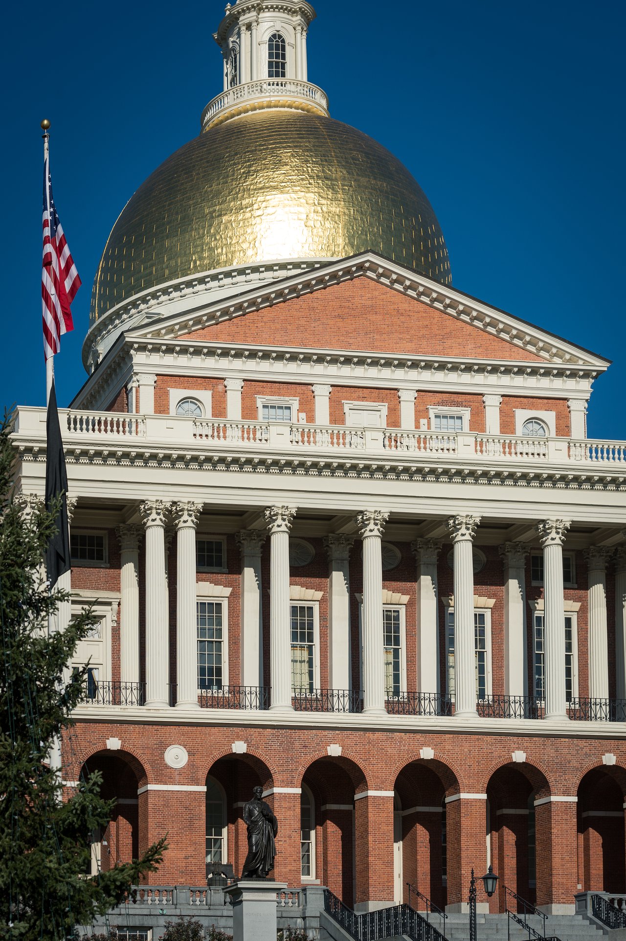 The Massachusetts State House with its golden dome, red brick facade, and white columns under a clear blue sky.
