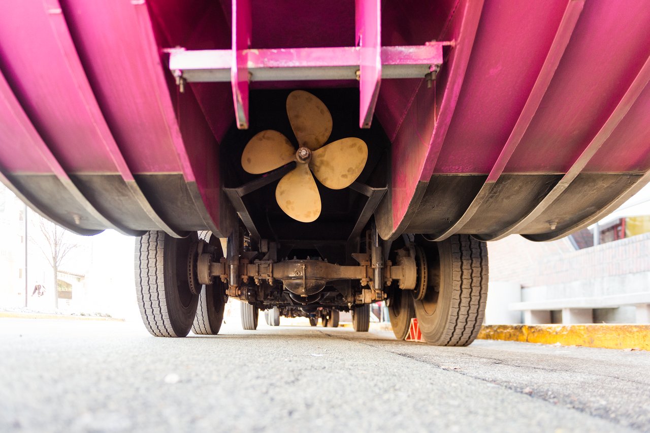 Close-up view of the underside of a Boston Duck Tour vehicle, showing its wheels, axle, and propeller.