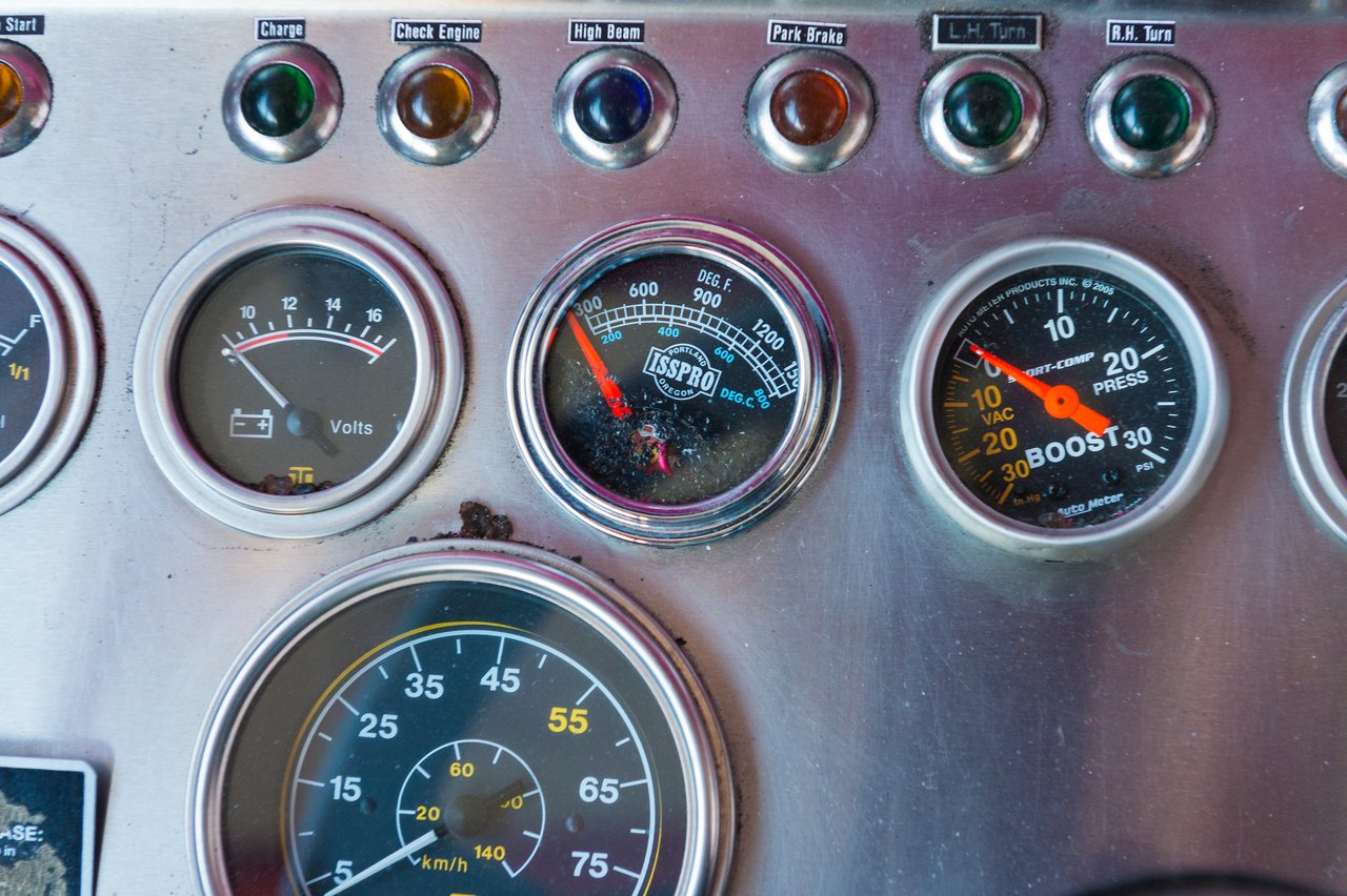 Close-up of a vehicle dashboard with multiple gauges and indicator lights, including speed, voltage, temperature, and boost pressure.