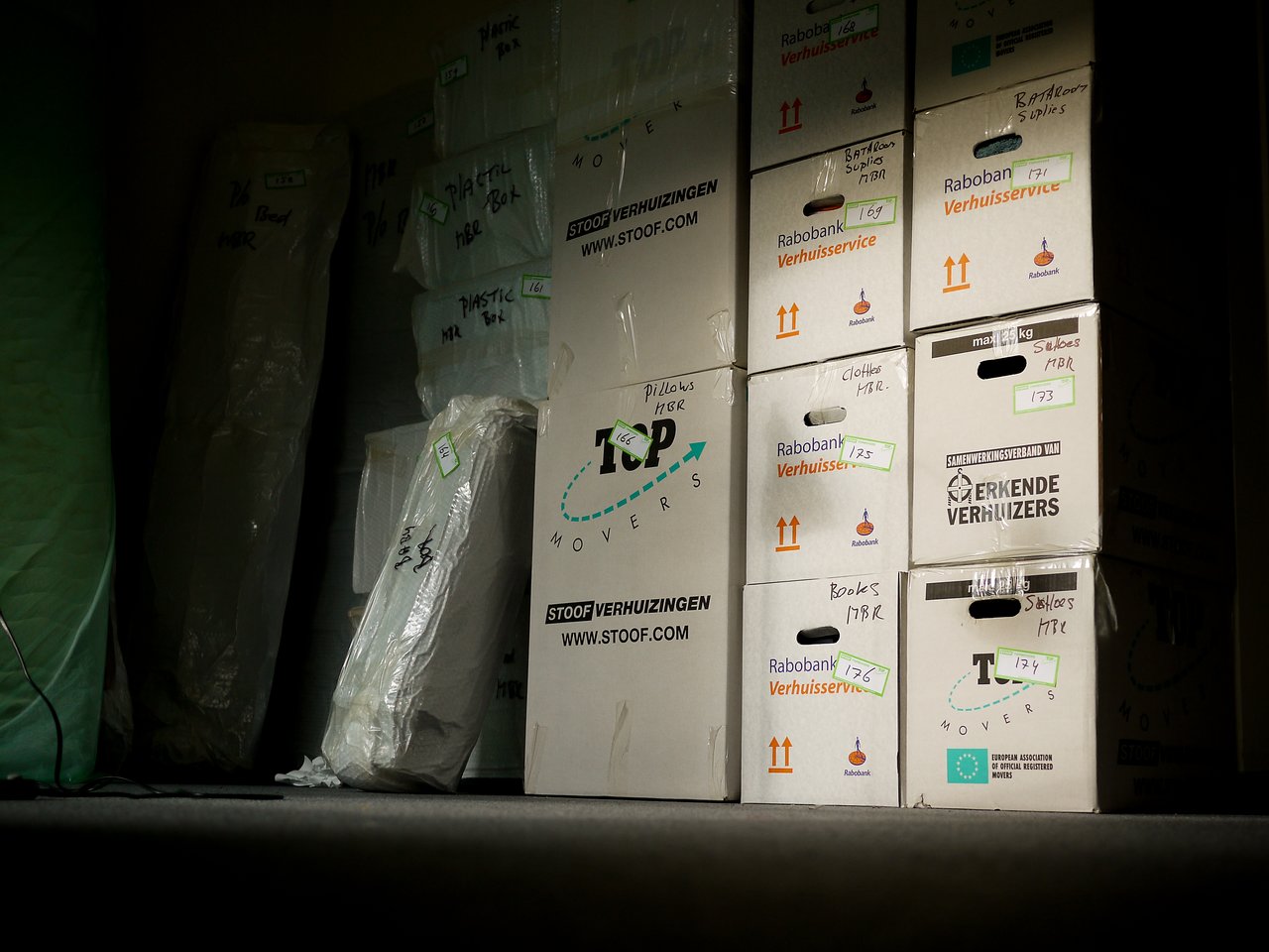 Stacked and labeled moving boxes in a dimly lit space, prepared for relocation.