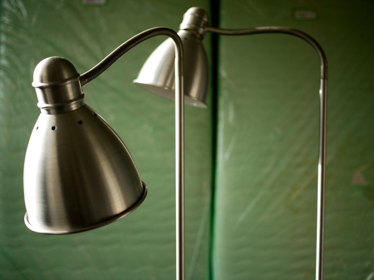 Two metal floor lamps with adjustable necks stand in front of a green padded background.