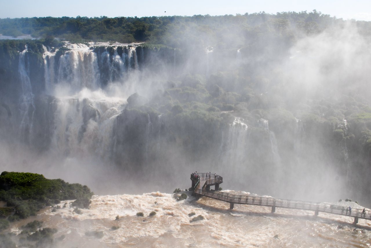 Visitors stand on a viewing platform surrounded by mist, overlooking the powerful Iguazu Falls cascading down rocky cliffs.