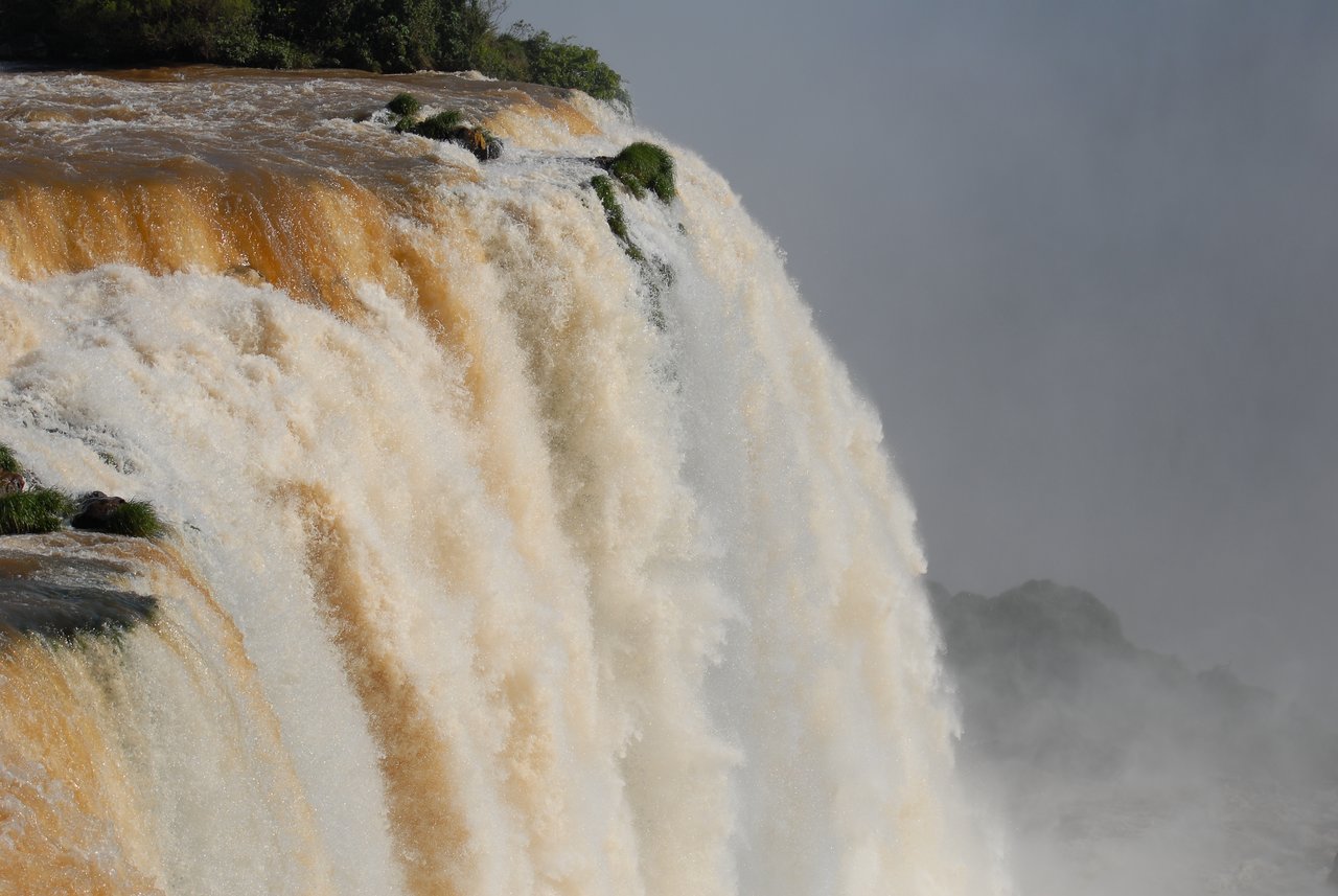 Water cascades over the edge of Iguazu Falls, creating a powerful flow with mist rising in the background.