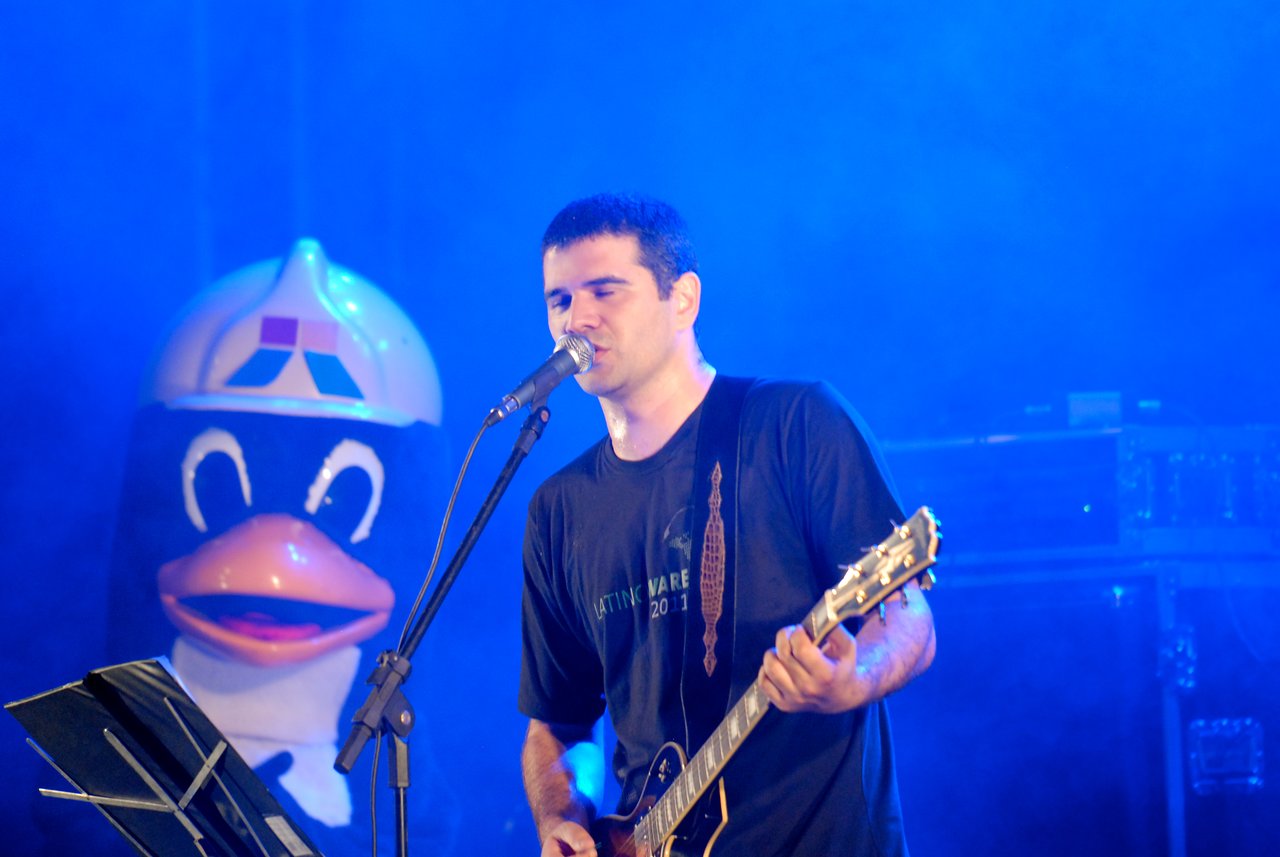 A musician sings into a microphone while playing an electric guitar on stage.