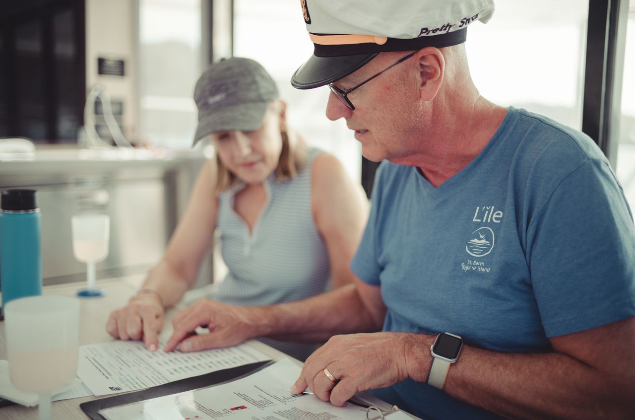 A man wearing a captain's hat and a woman review documents together at a table on a boat.
