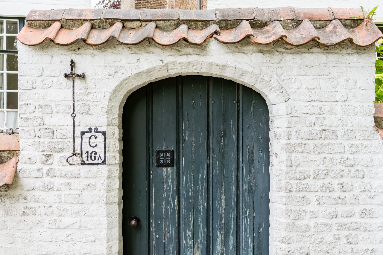 A weathered wooden door set in a white brick wall with a small sign and metal cross beside it.