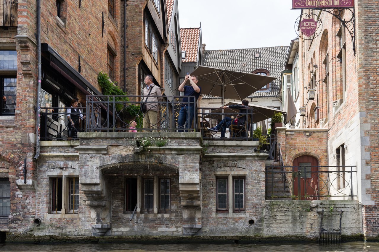 People stand on a terrace overlooking the water, with one person taking a photo.