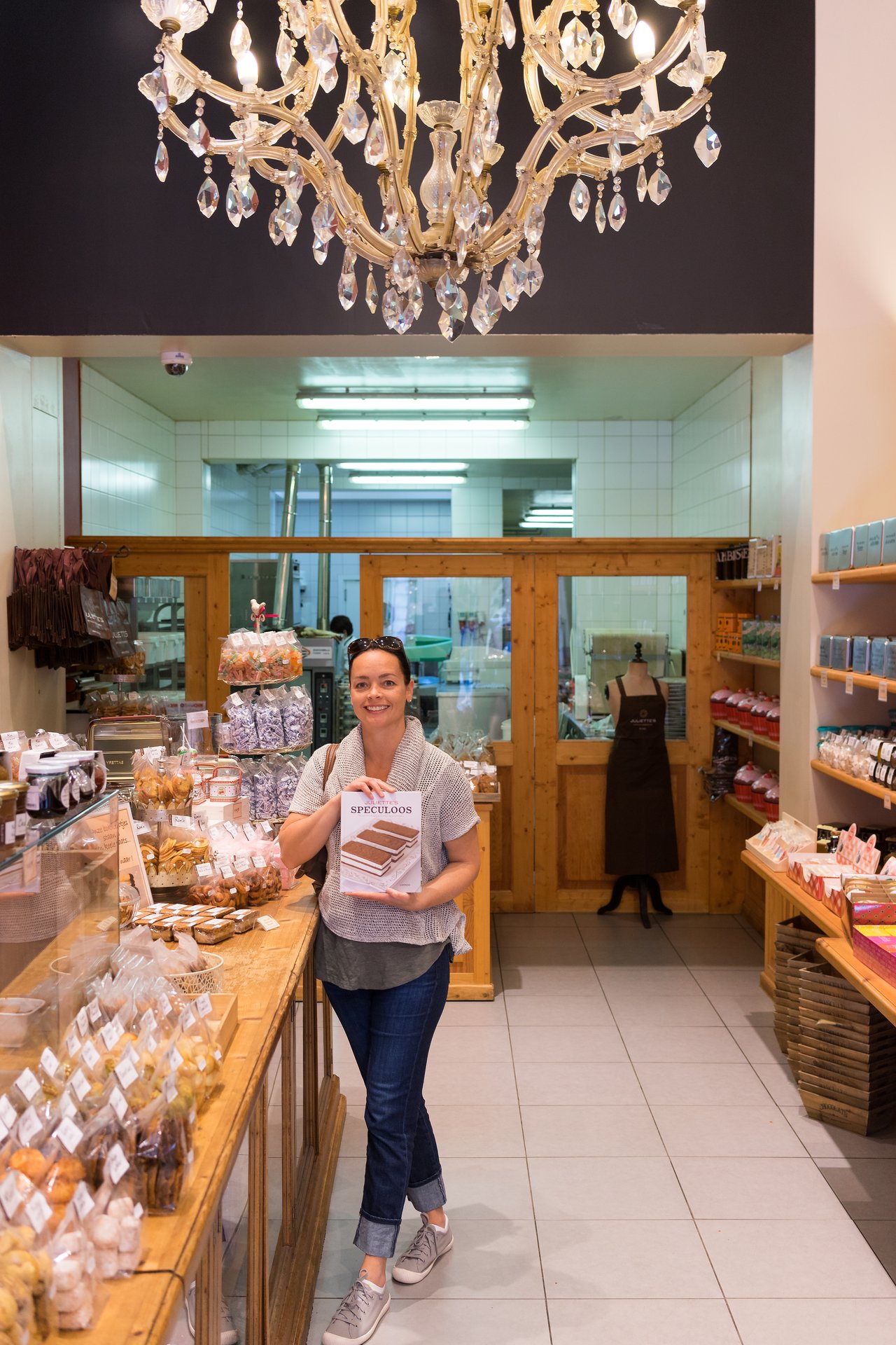 A woman stands in a bakery, smiling and holding a book titled "Speculoos.