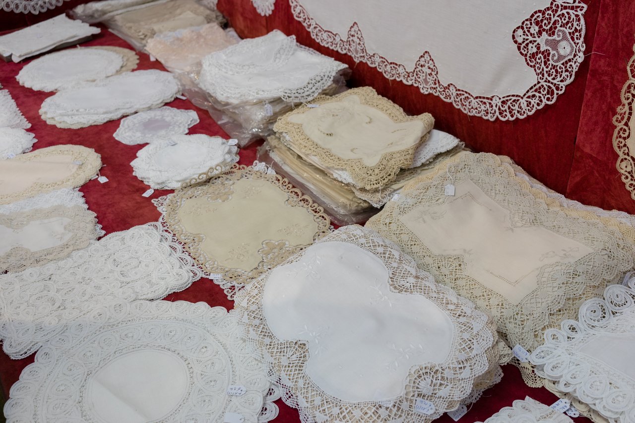 Various lace doilies and table linens displayed on a red fabric surface, featuring intricate patterns and delicate edges.
