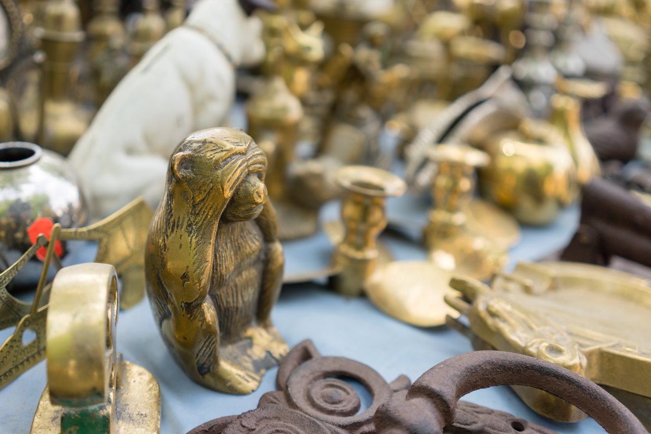 A market stall displaying brass antiques, including a small brass monkey figurine covering its eyes.