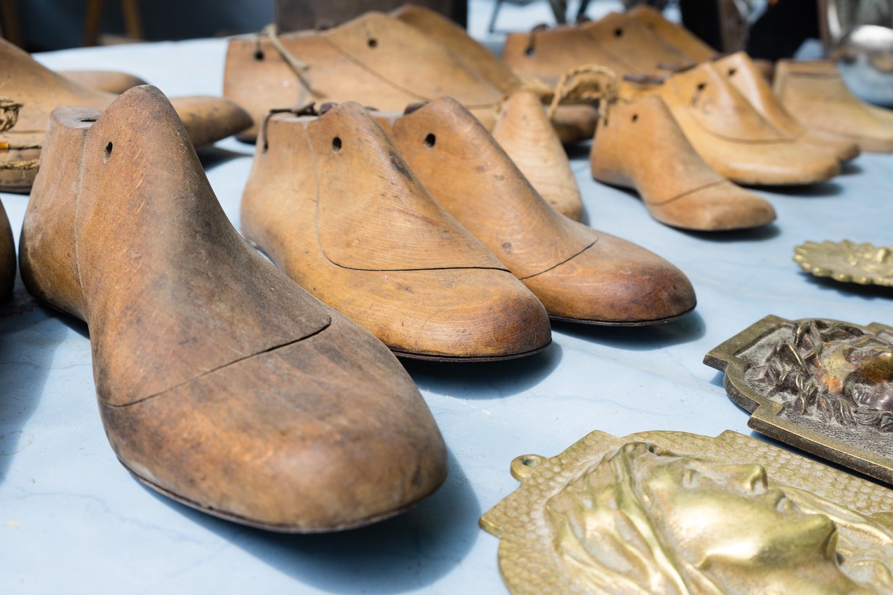 Wooden shoe molds and brass ornaments displayed on a market table in Bruges.