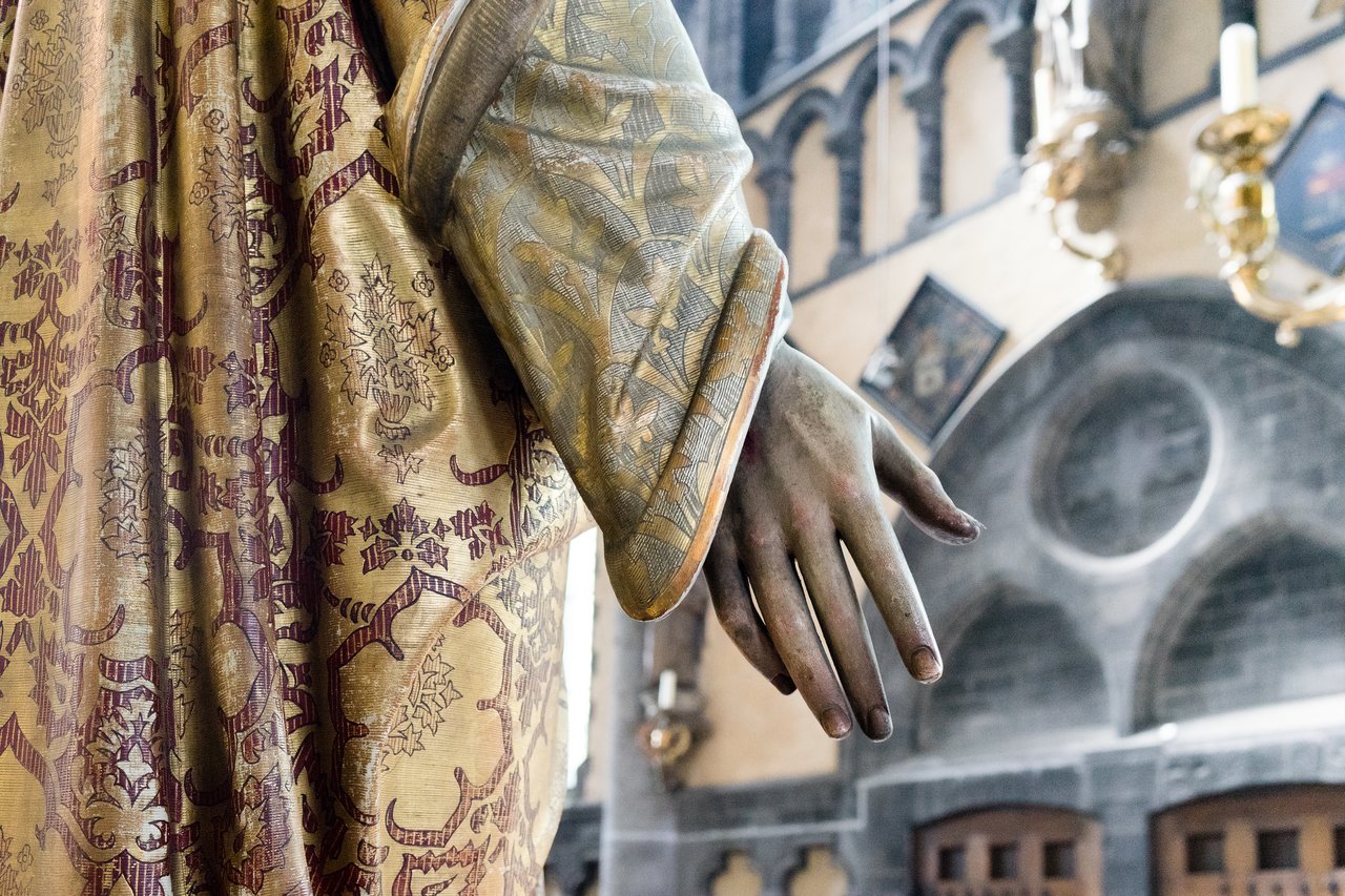 Close-up of a statue's hand in an ornate robe inside Our Lady Church in Bruges.