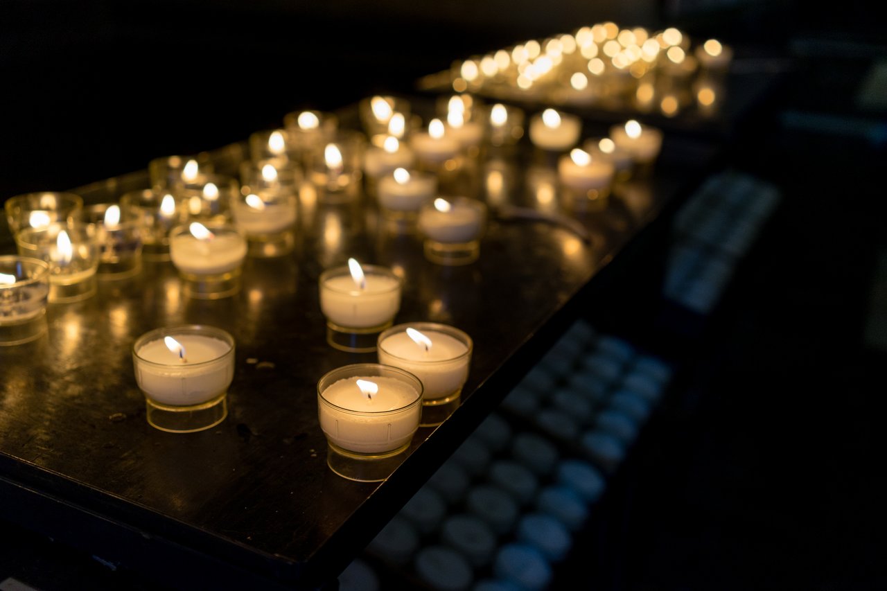 Lit votive candles on a dark table inside Our Lady Church, with unlit candles stored below.