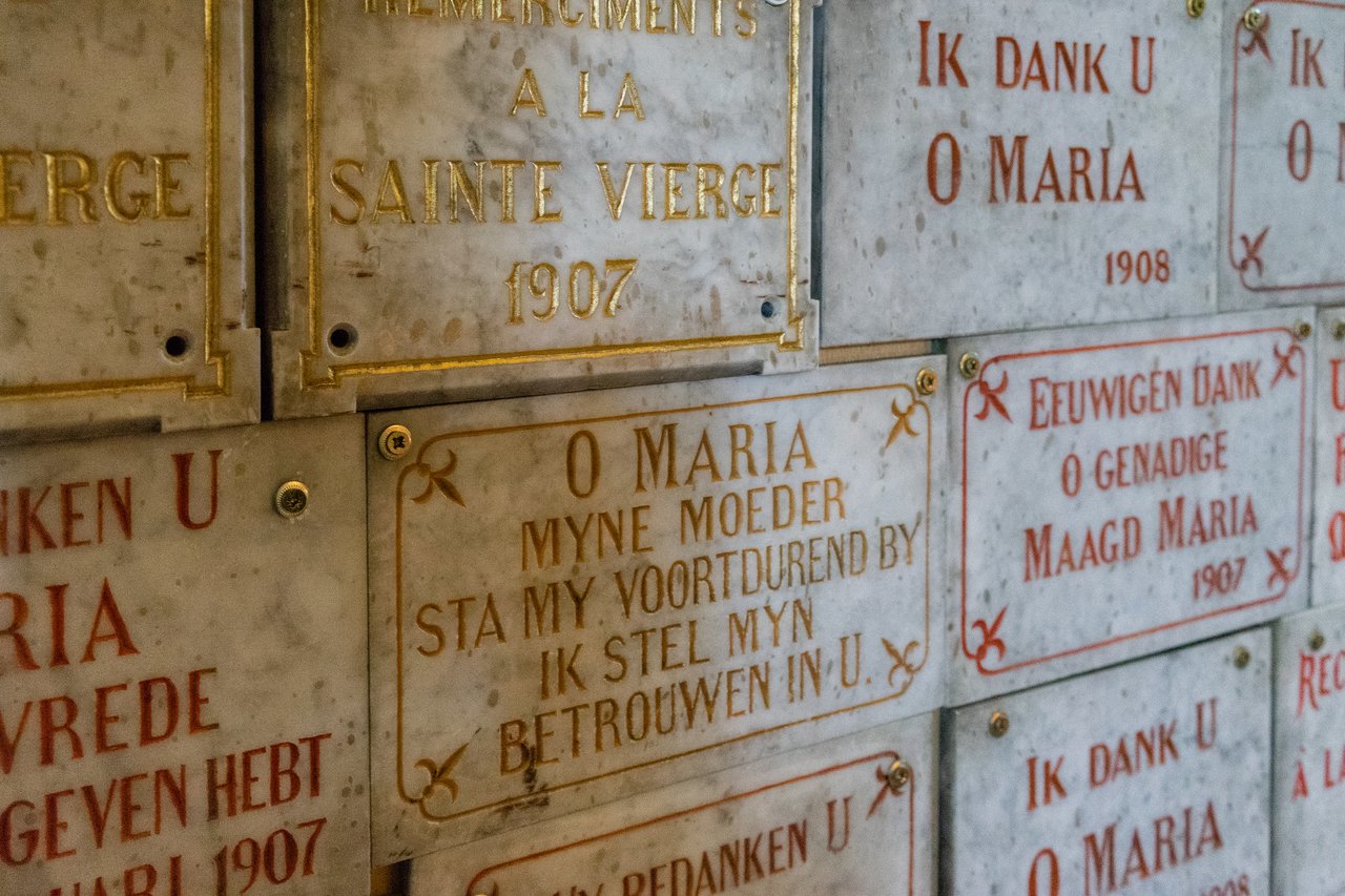 A wall with marble plaques featuring inscriptions in Dutch and French, expressing gratitude to the Virgin Mary.