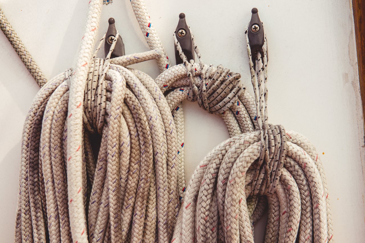 Coiled sailing ropes neatly hung on hooks against a white surface.
