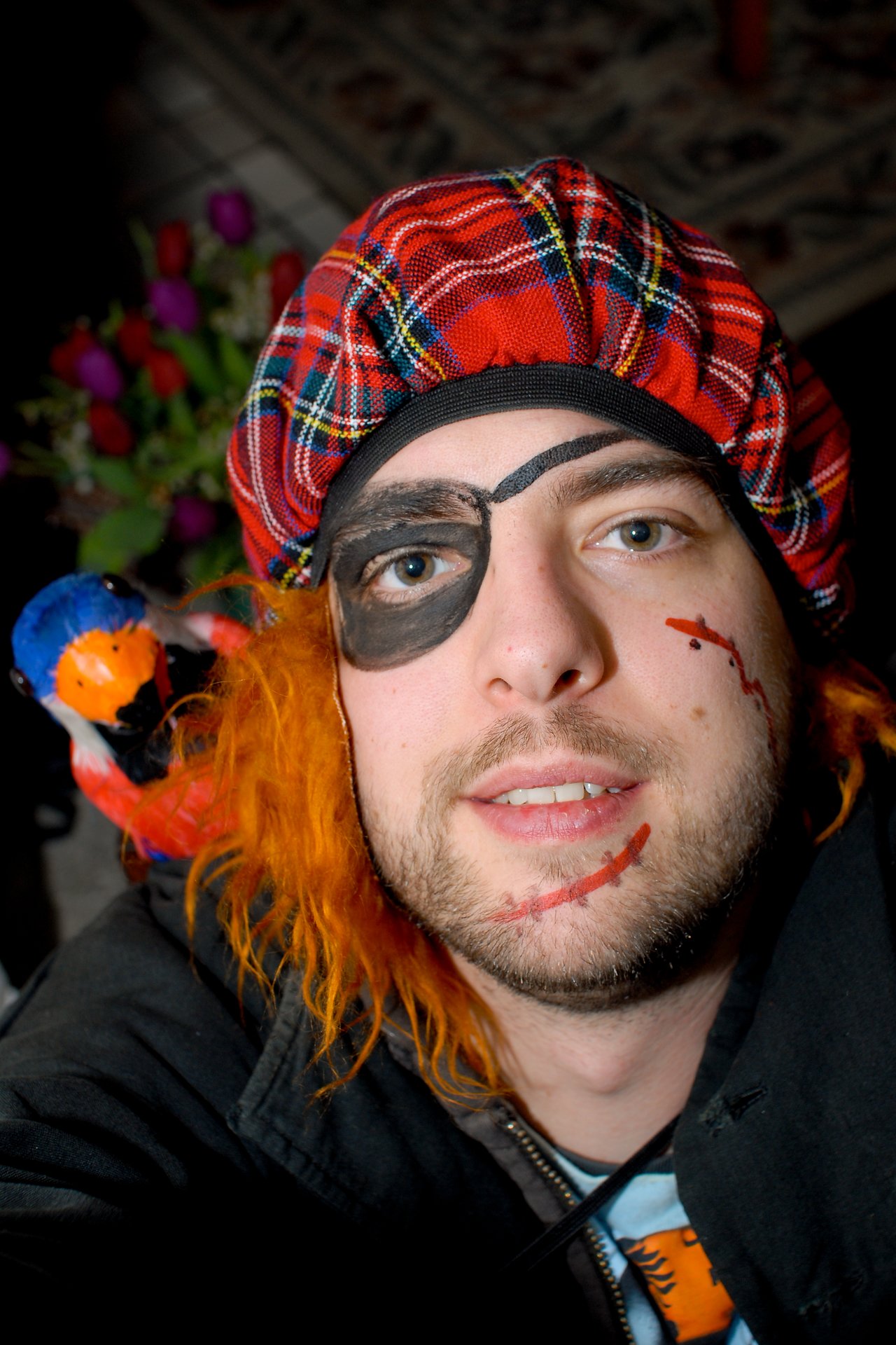 Person dressed as a pirate with a red plaid hat, fake eye patch, and toy parrot on their shoulder.