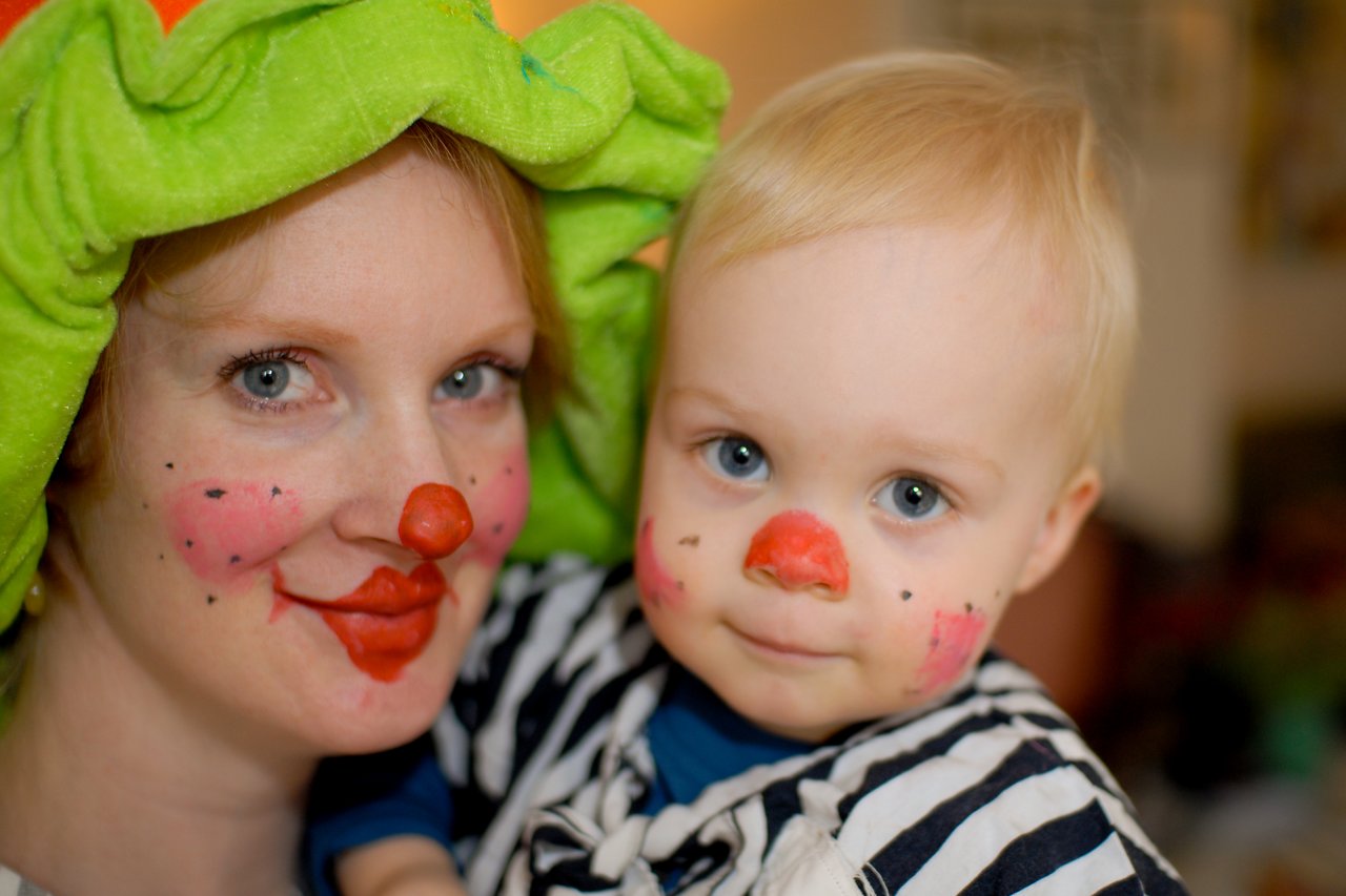 A woman and a baby dressed as clowns with painted faces and red noses, smiling at the camera.