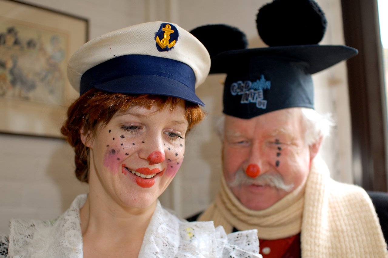 Two people in festive costumes with clown makeup smile during a Carnaval celebration.