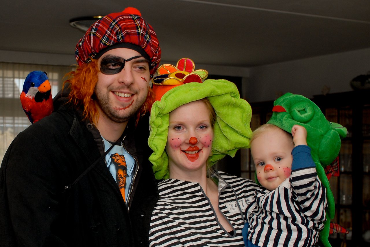 Three people and a child in colorful costumes and face paint smile at the camera, dressed for a carnival celebration.