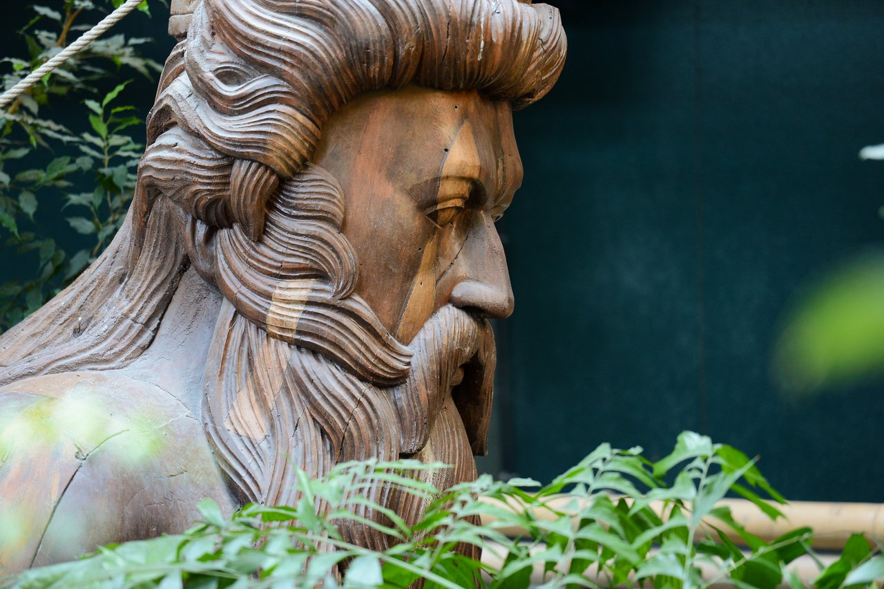 A large wooden sculpture of a bearded man's face, partially surrounded by green plants.