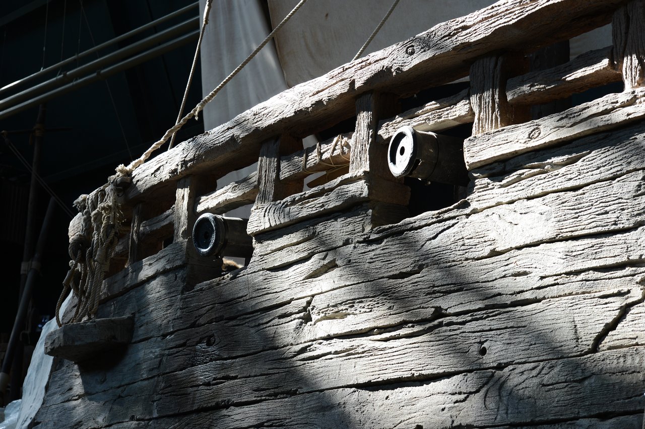 Close-up of a wooden ship replica with small cannons sticking out from the sides, illuminated by sunlight.