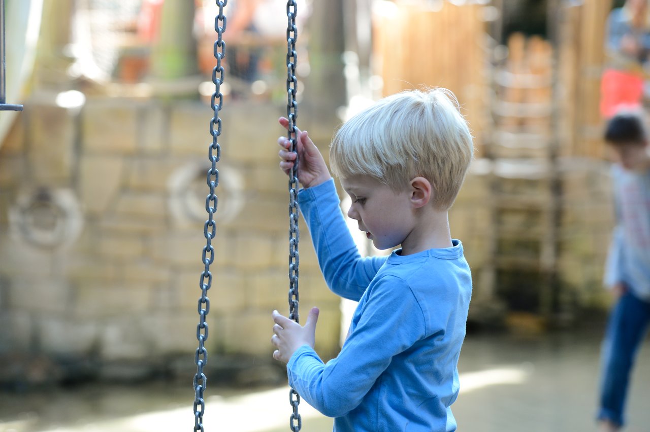 A young child in a blue shirt holds onto chains while playing at an outdoor playground.