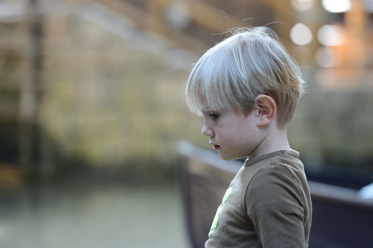 A young child with blond hair and a brown shirt looks down with a focused expression.
