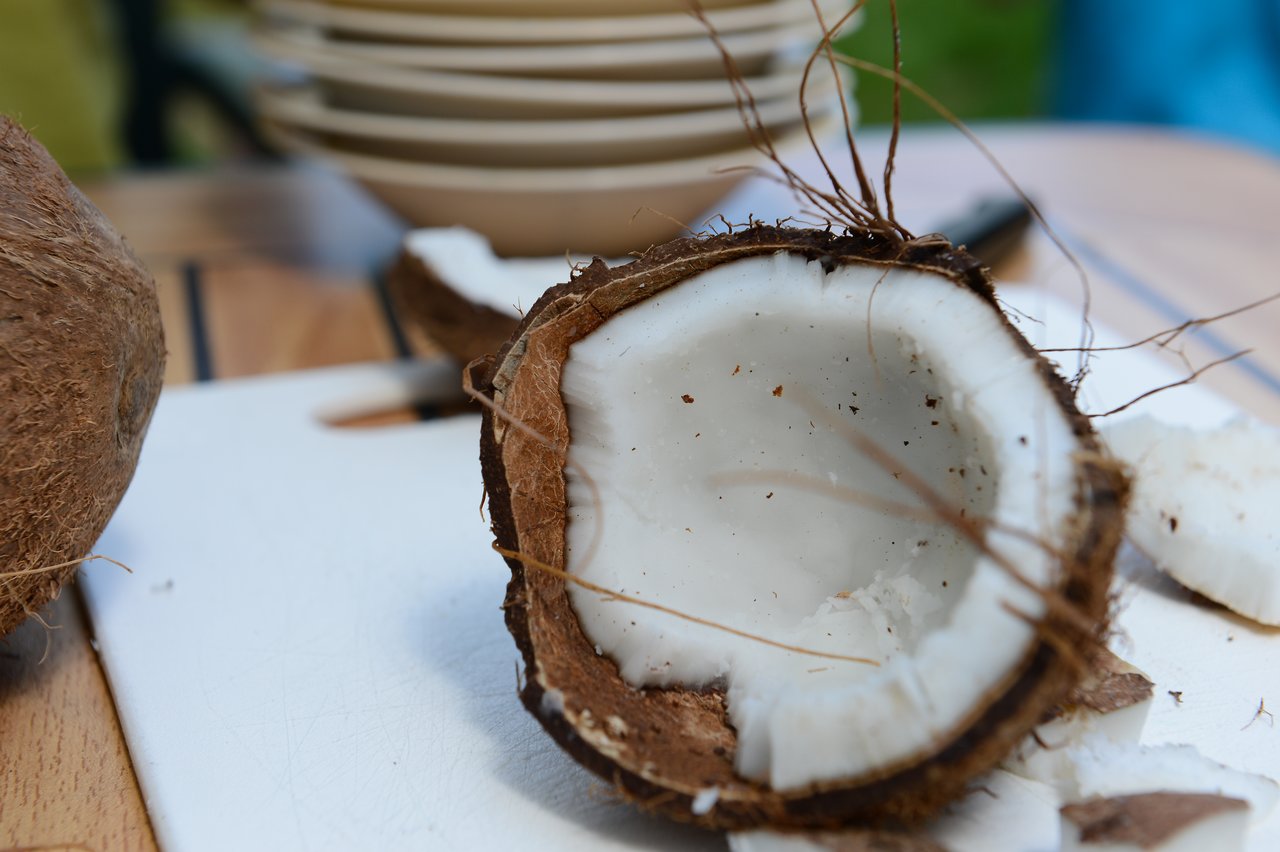 A freshly cracked coconut on a cutting board, with plates stacked in the background.