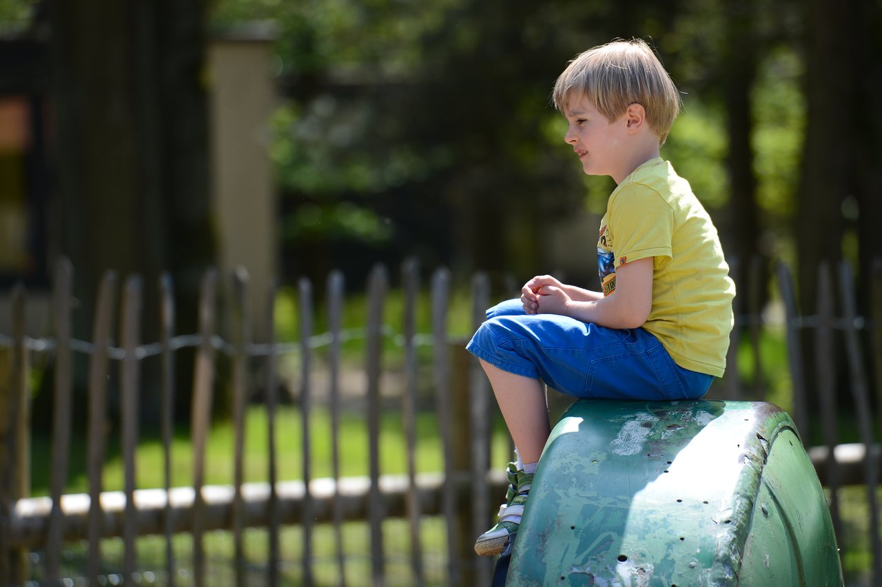 A young boy in a yellow shirt sits on a green playground structure, looking to the side.