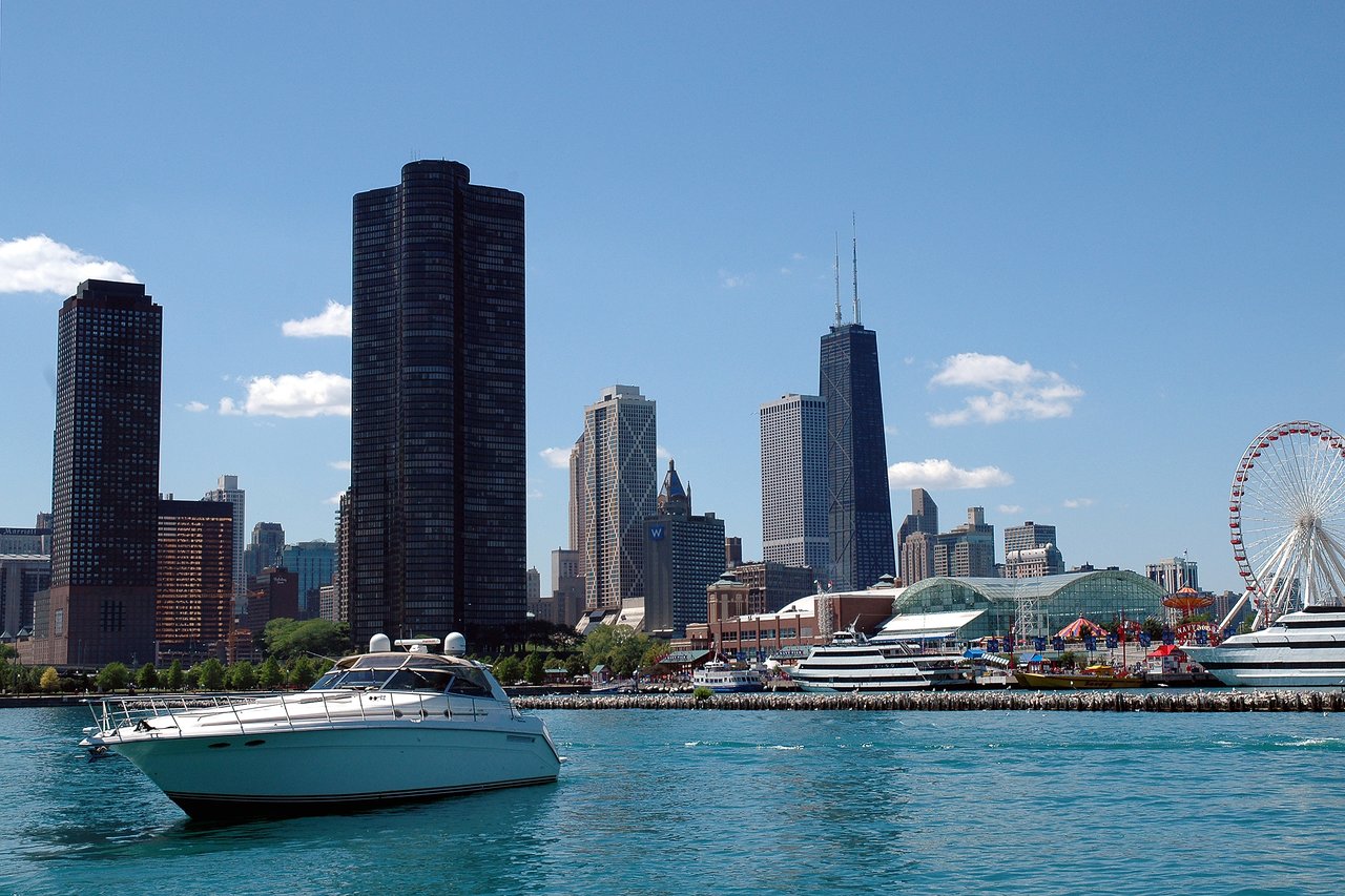 A white boat floats on the water with a city skyline and Ferris wheel in the background.