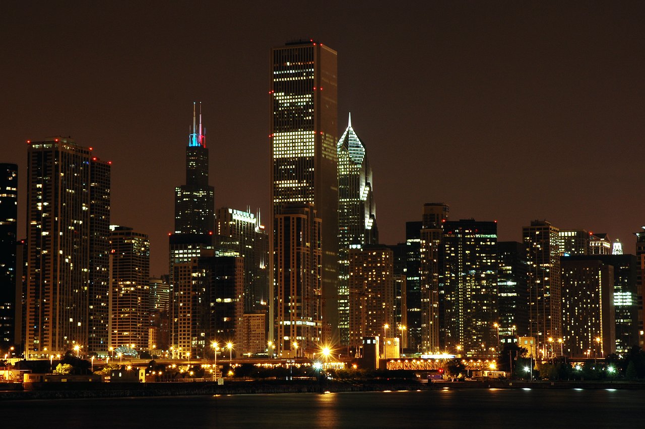 Chicago skyline at night with illuminated skyscrapers and city lights reflecting on the water.